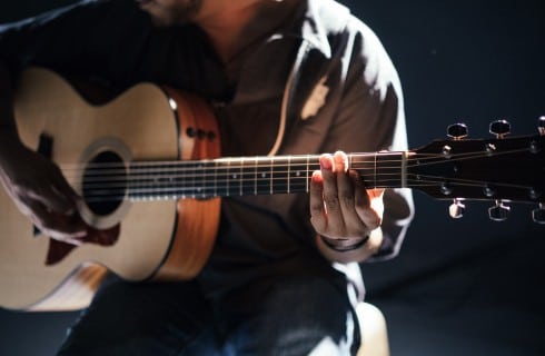 Man sitting on a stool playing a guitar