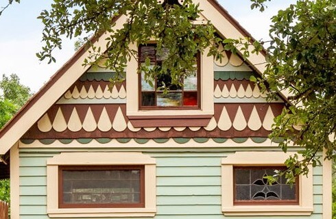 Outside of tiny house with multicolored siding and stained glass windows.