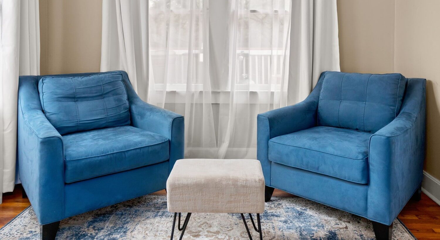 Two blue armchairs with a rug and foot rest.