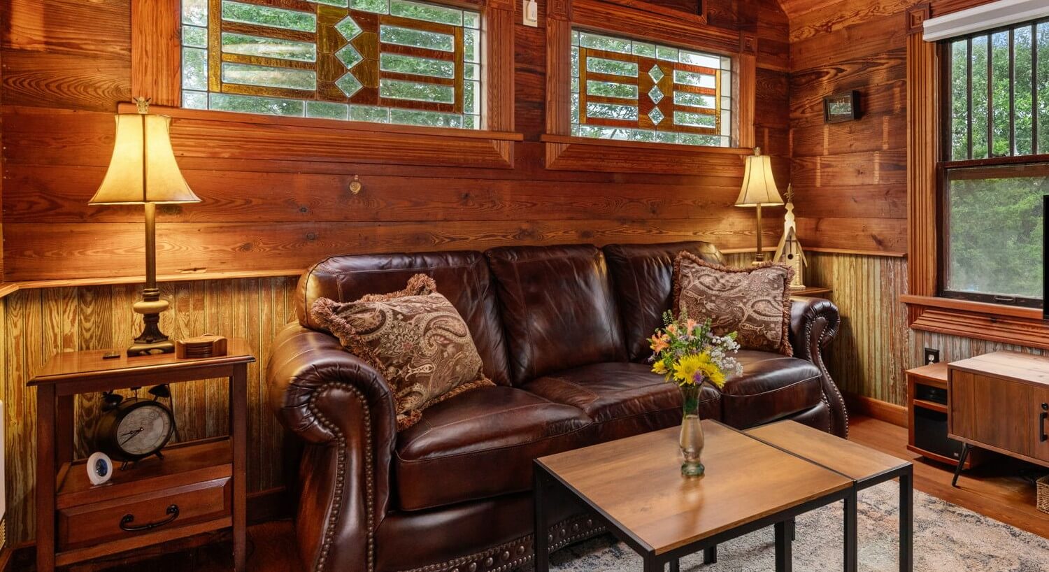 Inside of a tiny house with a leather couch and stained glass windows.