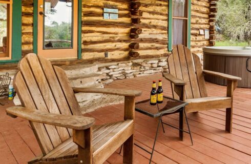 Exterior porch of log cabin with two chairs and a hot tub.