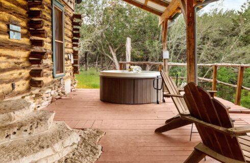 Log cabin exterior with two chairs and a hot tub.