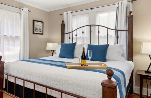 King size bed with white bead spread and a tray with a bottle of wine and two glasses.