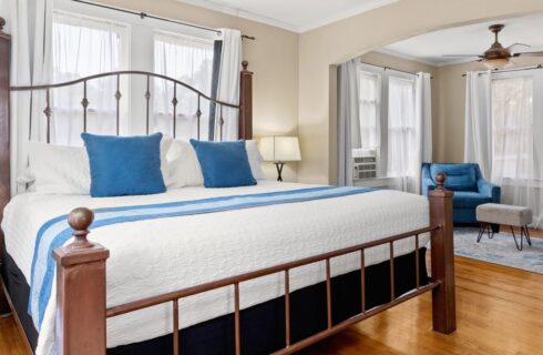 King size bed with white bedspread and an arched opening to a room with two blue chairs.
