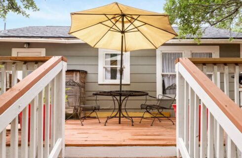 Large outdoor deck with gas grill, potted plants and wrought iron patio table with two chairs.