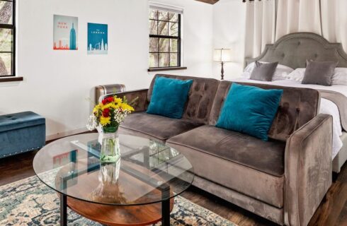 Inside of cabin with a couch and bed and flowers in a vase on a glass table.