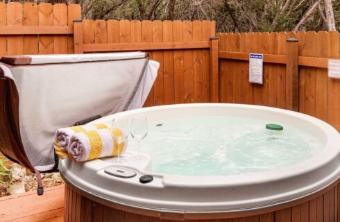 Hot tub surrounded by a wood fence with two yellow striped towels and two wine glasses on the side of the tub.