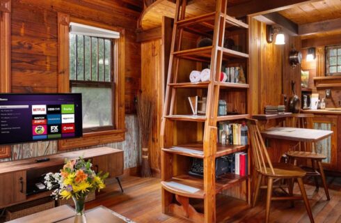 Interior of a tiny house with a ships ladder, TV and kitchen area.