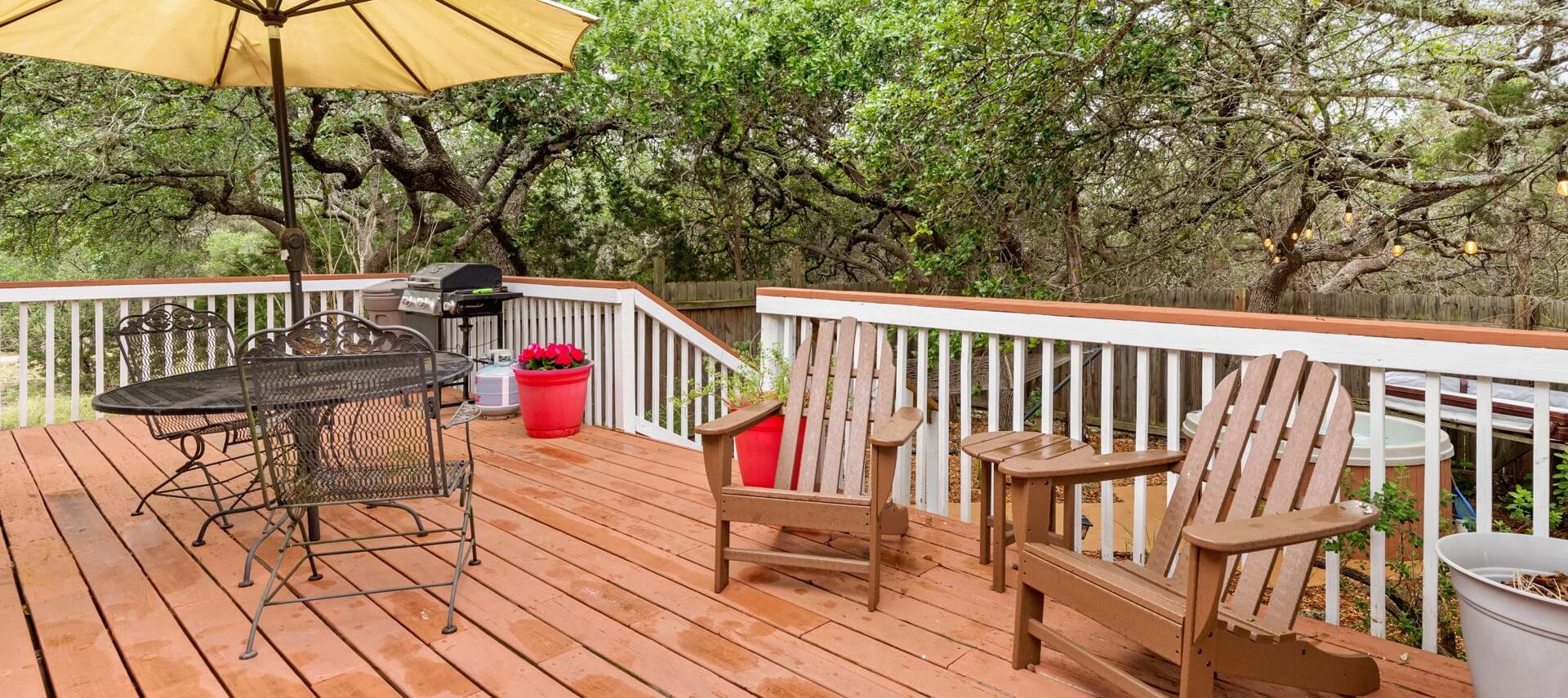 Deck with large oak trees and a patio table, BBQ grill and two chairs.
