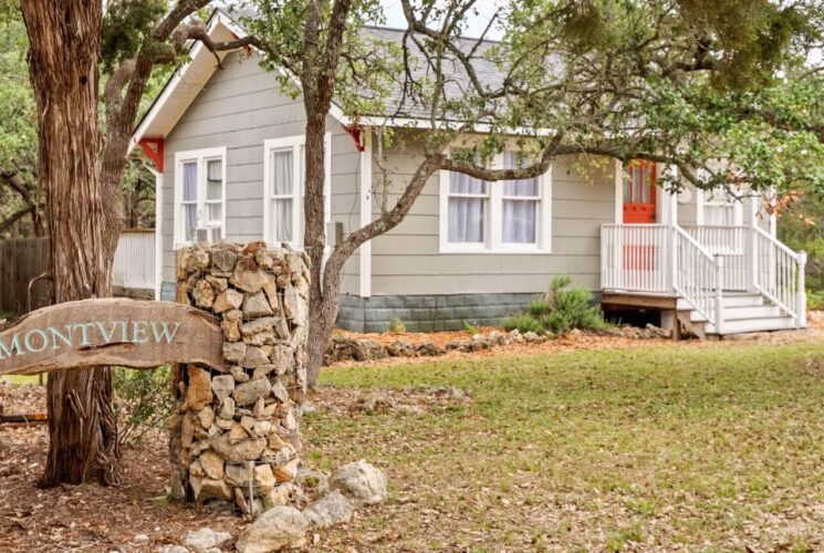 Small cottage nestled in the woods with a wood sign out front.