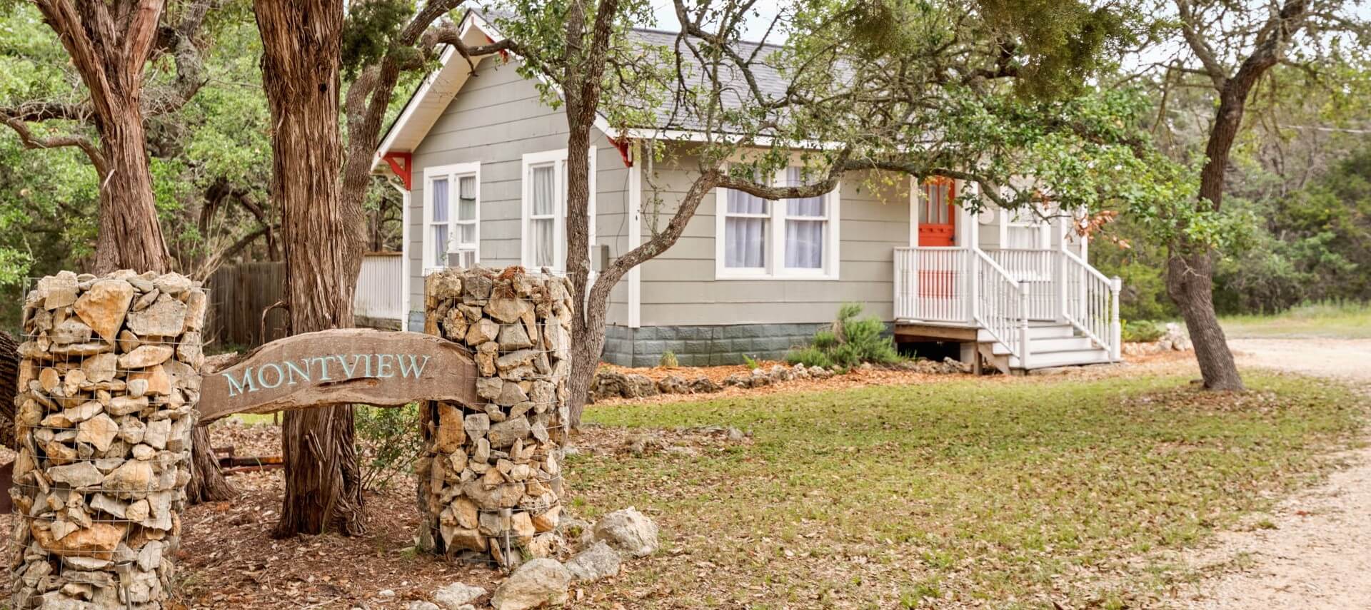 Small cottage nestled in the woods with a wood sign out front.