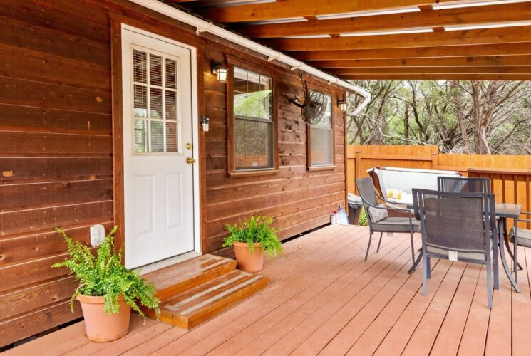 Cabin with wood siding, large front deck with overhang, nestled in the woods