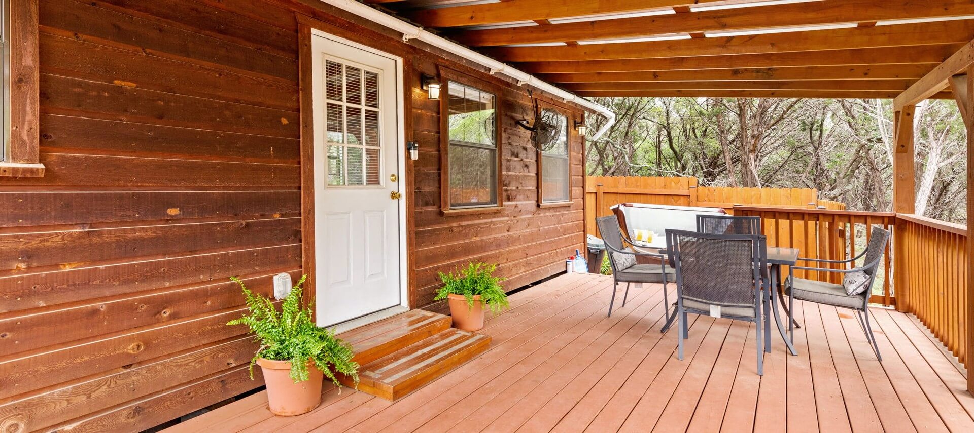 Cabin with wood siding, large front deck with overhang, nestled in the woods