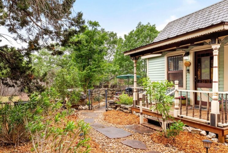 Small cabin with front porch, surrounded by trees, with side area with stone wall and round hot tub