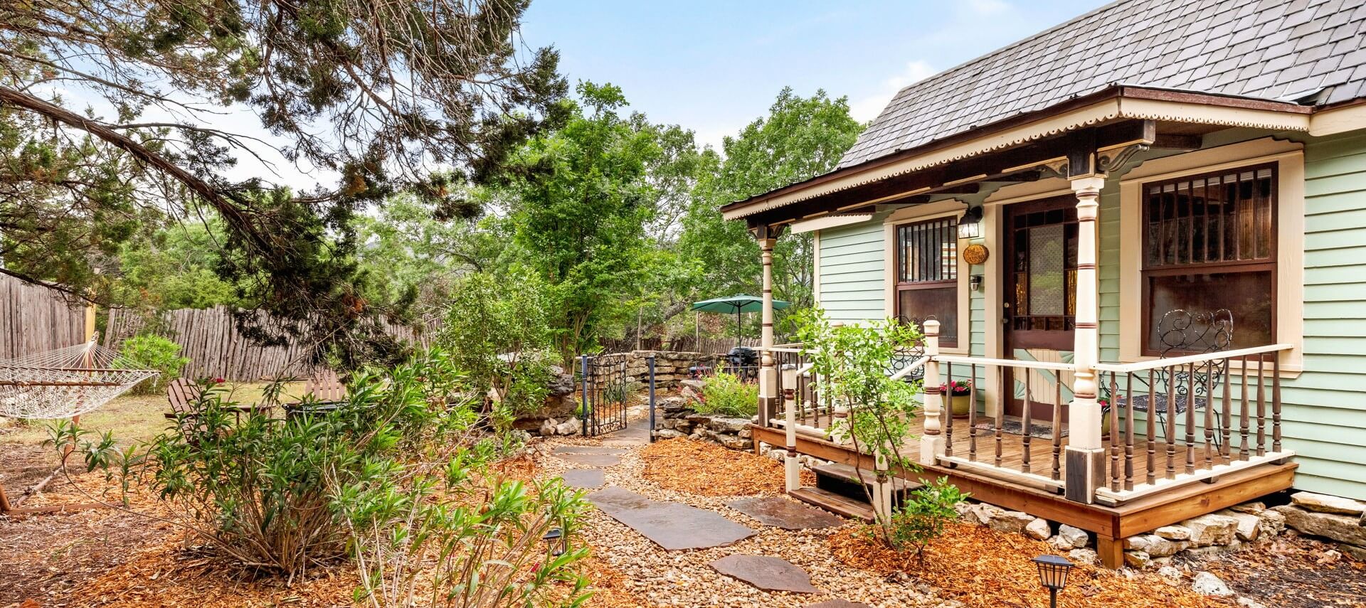 Small cabin with front porch, surrounded by trees, with side area with stone wall and round hot tub