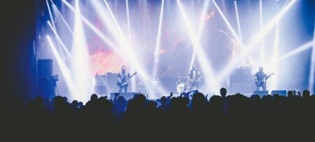 Image shows a concert at night with lights illuminating the musicians and the crown with their hands in the air.