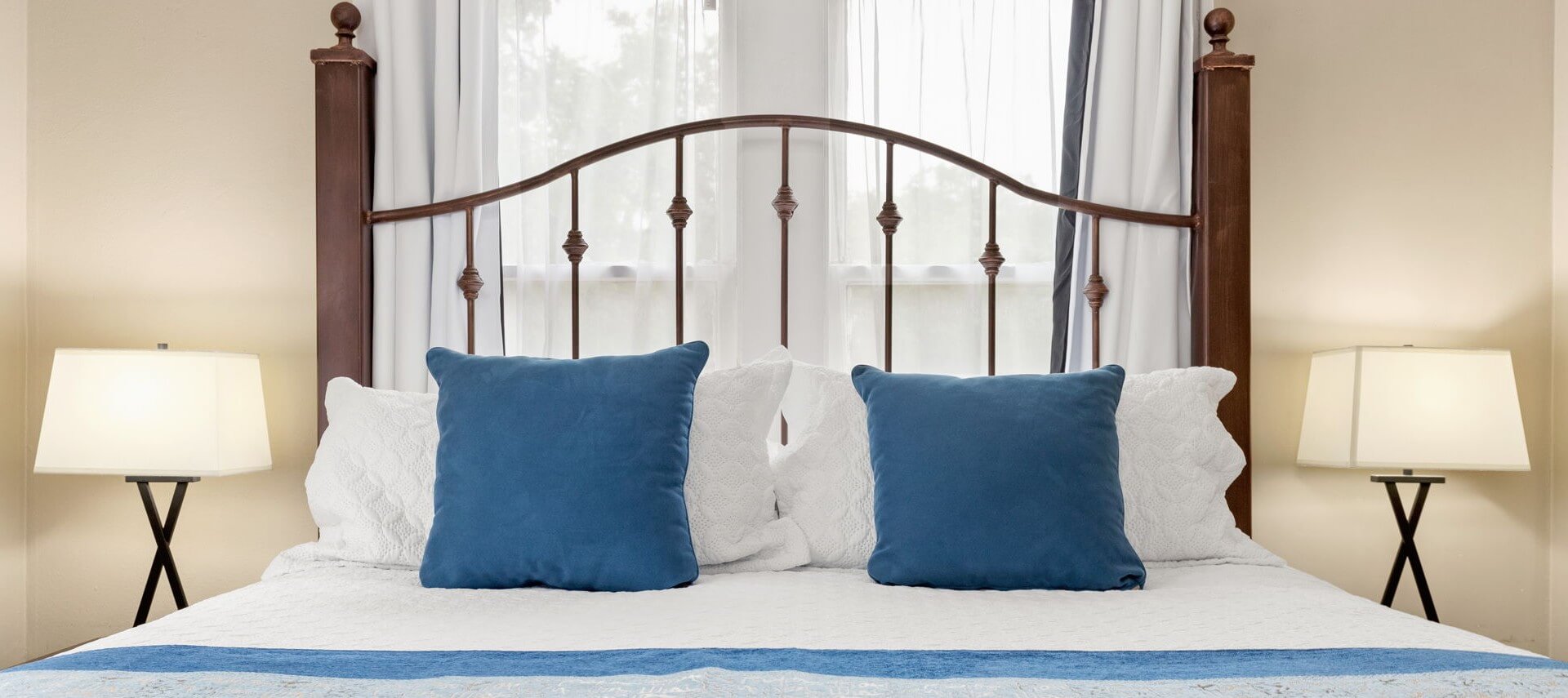King size bed with blue pillows and white bed spread and two lamps.