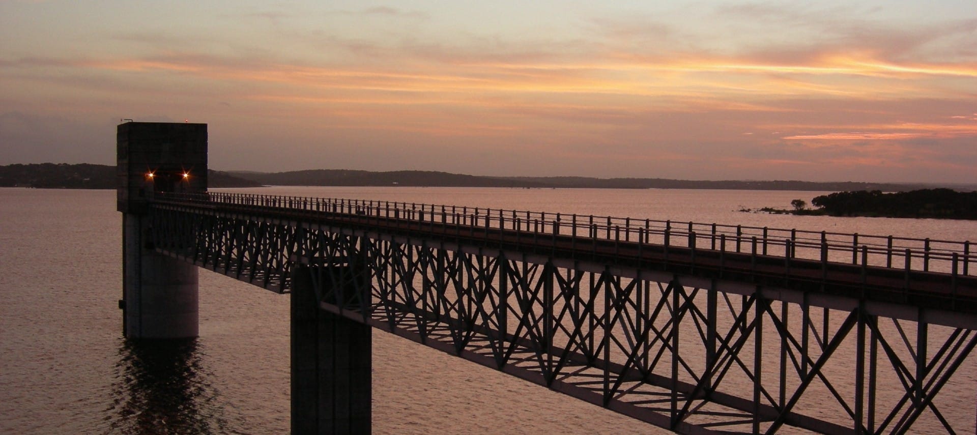 Long walkway over an expansive body of water with sunset skies