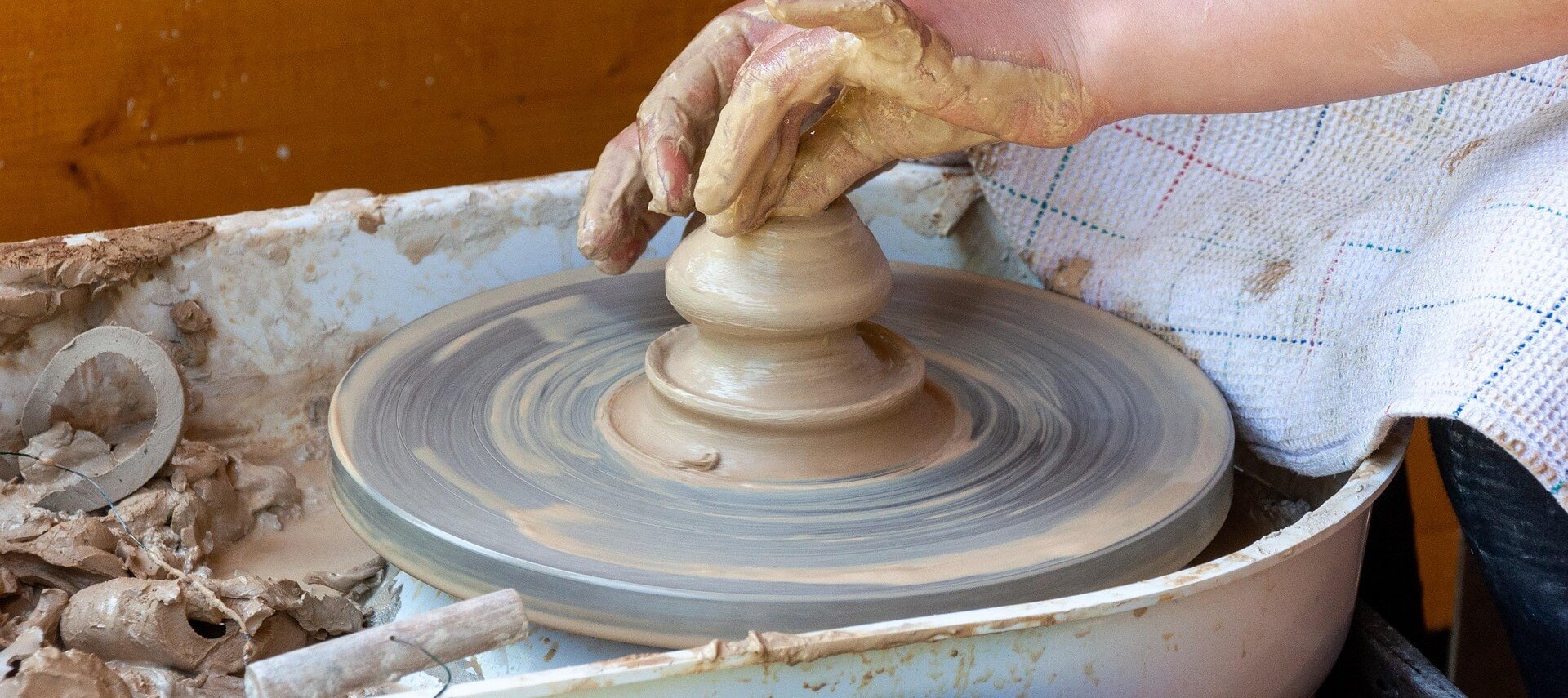 A picture of an artist forming clay with their hands on a potters wheel.