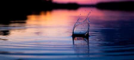 A pebble thrown into the water as the sun sets with pastel colors reflected off the water.