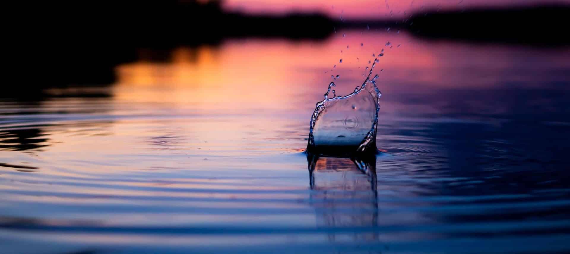 A pebble thrown into the water as the sun sets with pastel colors reflected off the water.